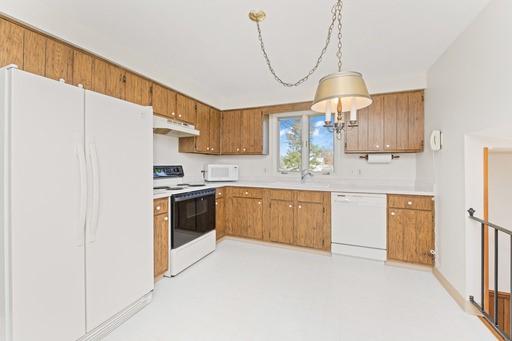 kitchen with brown cabinets, light countertops, a sink, under cabinet range hood, and white appliances