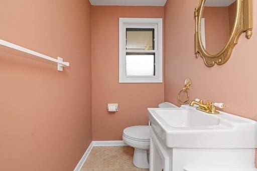 half bath featuring baseboards, tile patterned floors, toilet, and vanity