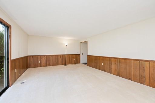 carpeted empty room with a wainscoted wall and wooden walls