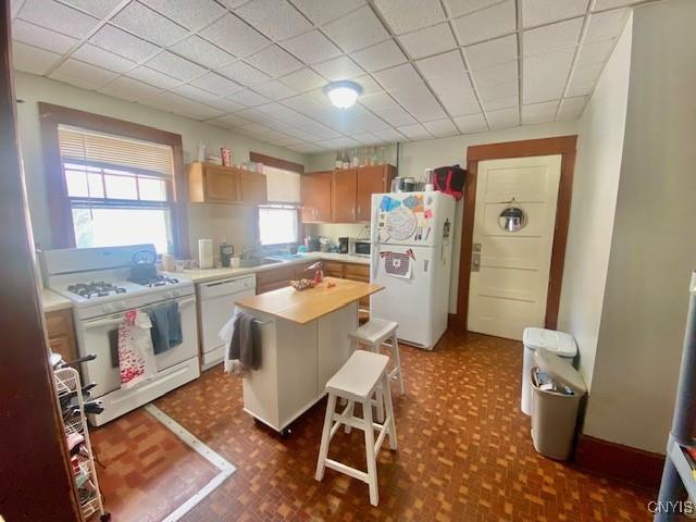 kitchen featuring a center island, light countertops, dark floors, a drop ceiling, and white appliances