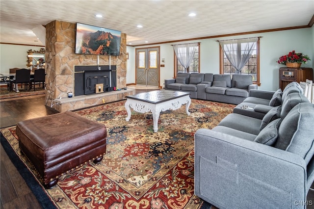 living area with crown molding, recessed lighting, wood finished floors, and a stone fireplace