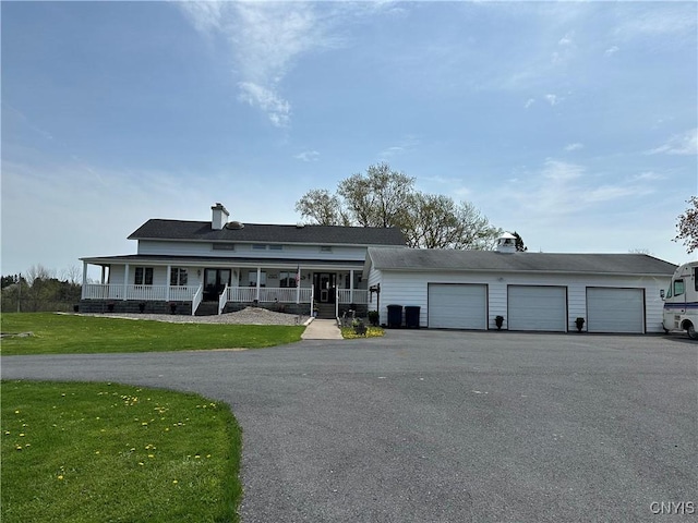 view of front facade with a front lawn, covered porch, a chimney, an attached garage, and driveway