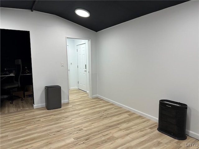 unfurnished room featuring baseboards, light wood finished floors, and lofted ceiling