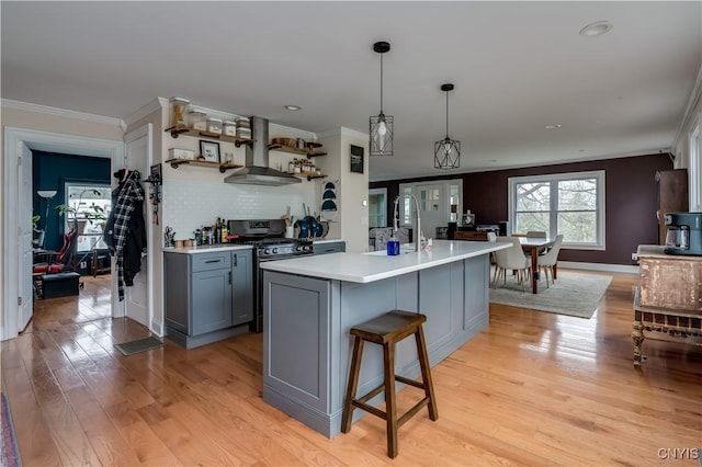 kitchen with crown molding, stainless steel gas stove, light countertops, gray cabinets, and wall chimney exhaust hood