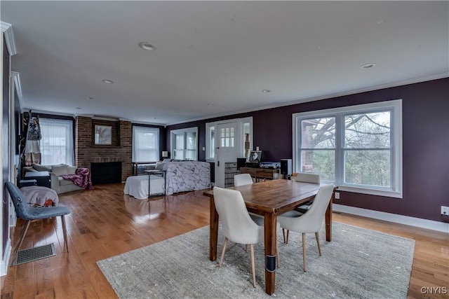 dining space featuring crown molding, visible vents, a fireplace, baseboards, and light wood-type flooring