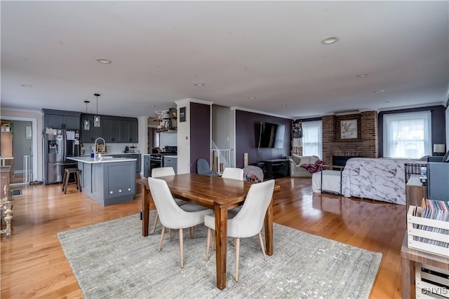 dining area featuring ornamental molding, light wood-style flooring, and a brick fireplace