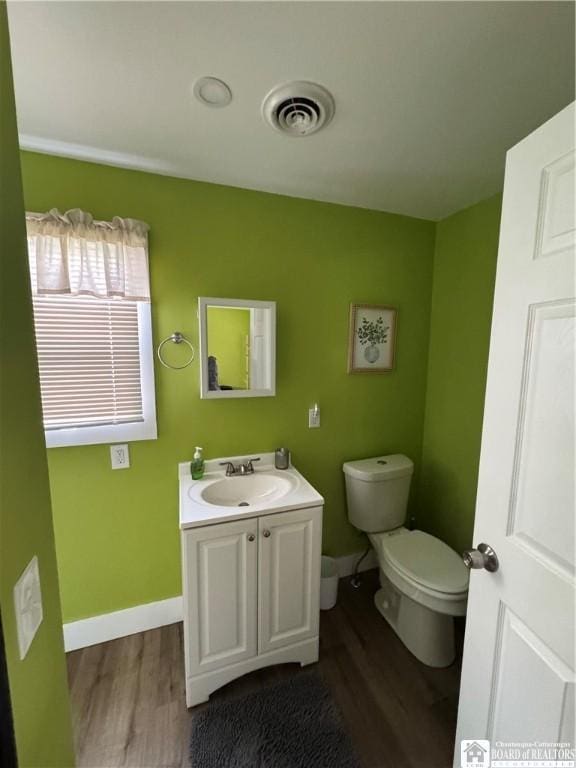 half bath featuring toilet, baseboards, visible vents, and wood finished floors