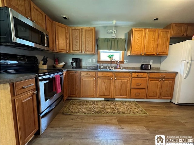 kitchen with brown cabinets, a sink, appliances with stainless steel finishes, and wood finished floors