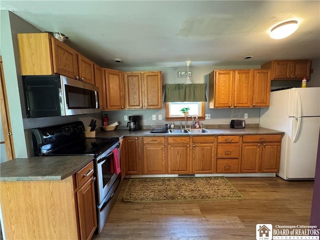 kitchen featuring stainless steel appliances, brown cabinetry, a sink, and wood finished floors