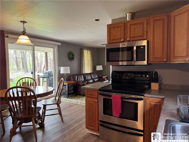 kitchen featuring light wood-style floors, appliances with stainless steel finishes, brown cabinets, and hanging light fixtures