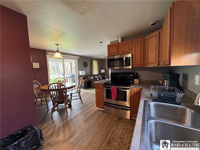 kitchen featuring light wood-type flooring, brown cabinets, a sink, hanging light fixtures, and stainless steel appliances