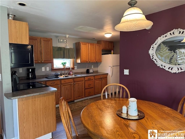 kitchen with freestanding refrigerator, black microwave, dark countertops, brown cabinets, and a sink