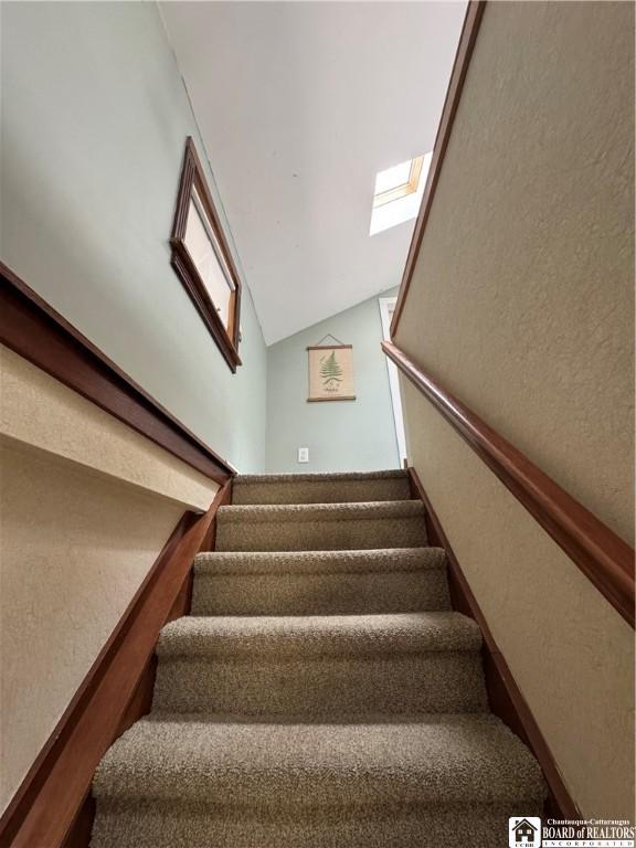 stairway with a textured wall and vaulted ceiling with skylight