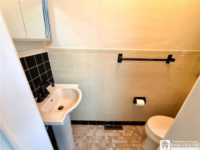 half bath with a sink, tile walls, a wainscoted wall, and toilet