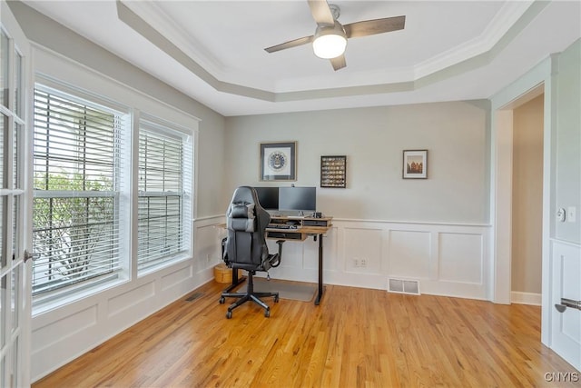 office area with visible vents, a decorative wall, ceiling fan, a raised ceiling, and light wood finished floors