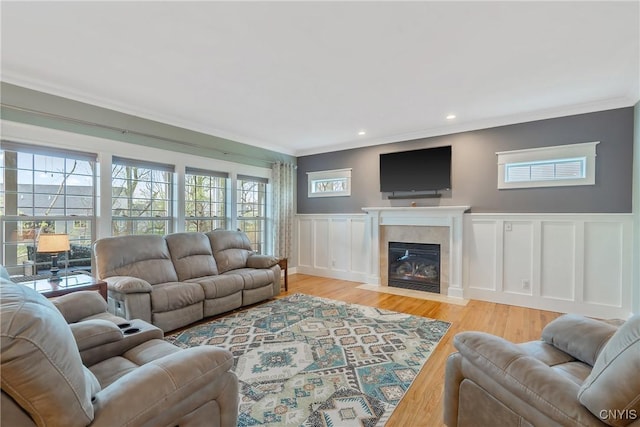 living room featuring a fireplace with flush hearth, wood finished floors, a wainscoted wall, ornamental molding, and a decorative wall