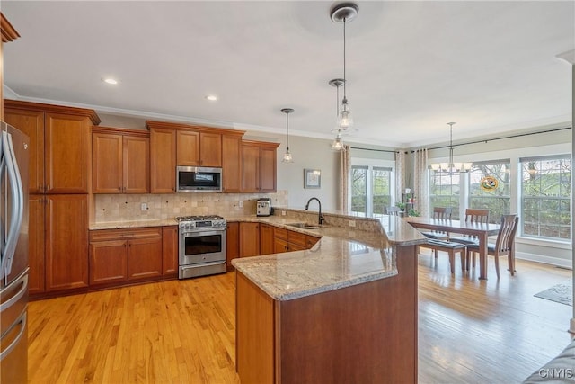 kitchen featuring brown cabinetry, crown molding, appliances with stainless steel finishes, a sink, and a peninsula