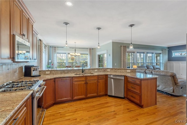 kitchen featuring appliances with stainless steel finishes, a sink, brown cabinetry, open floor plan, and a wealth of natural light