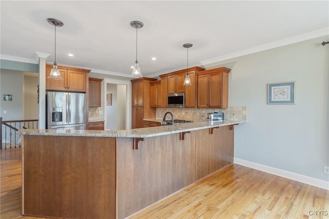 kitchen with brown cabinetry, a peninsula, light wood-style floors, light stone counters, and stainless steel appliances