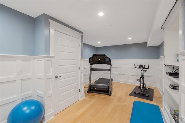 exercise room with a decorative wall, recessed lighting, wood finished floors, and a wainscoted wall