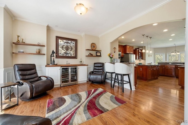 living room with crown molding, wine cooler, wood finished floors, arched walkways, and bar area