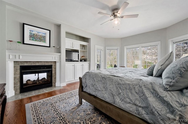 bedroom with ceiling fan, a tiled fireplace, and wood finished floors