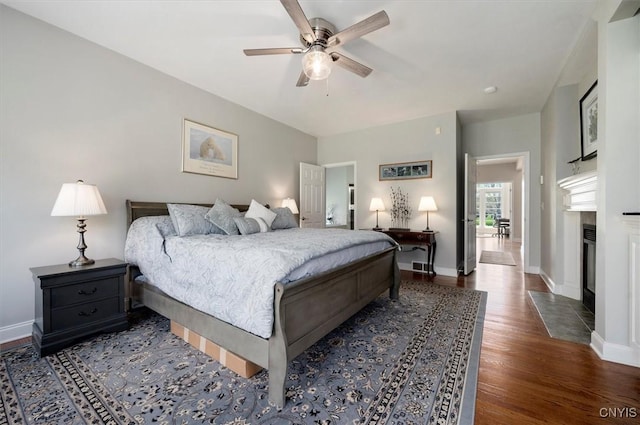 bedroom featuring a fireplace with flush hearth, baseboards, ceiling fan, and wood finished floors