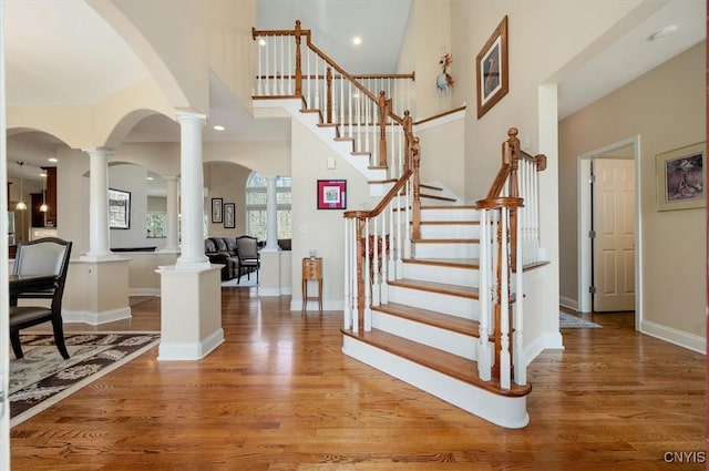 stairs featuring baseboards, arched walkways, decorative columns, and wood finished floors