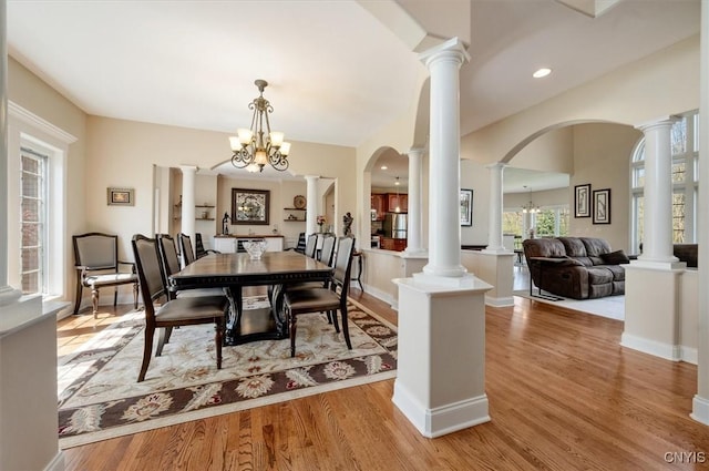 dining space featuring an inviting chandelier, arched walkways, light wood-style floors, and ornate columns