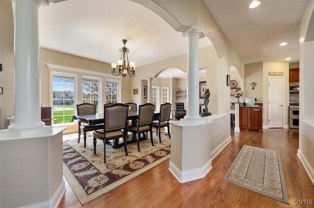 dining room featuring arched walkways, ornate columns, a notable chandelier, recessed lighting, and dark wood-type flooring