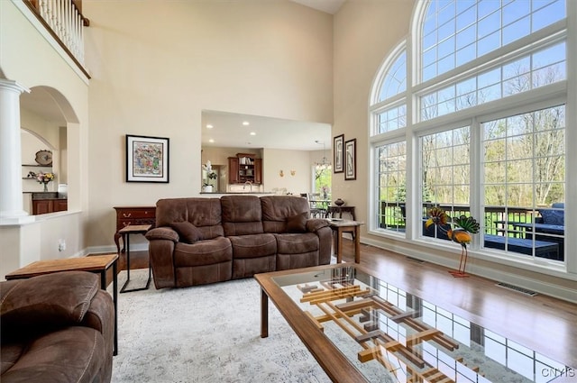 living room featuring visible vents, ornate columns, wood finished floors, and a towering ceiling