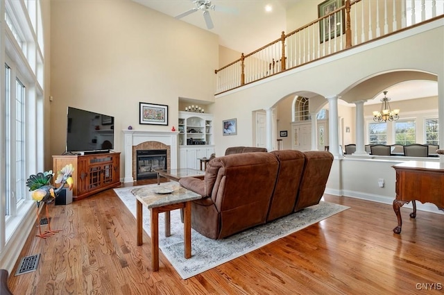 living room featuring a high ceiling, decorative columns, wood finished floors, and ceiling fan with notable chandelier