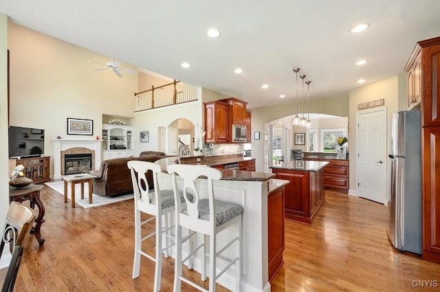 kitchen with a kitchen island, arched walkways, light wood finished floors, a peninsula, and stainless steel appliances