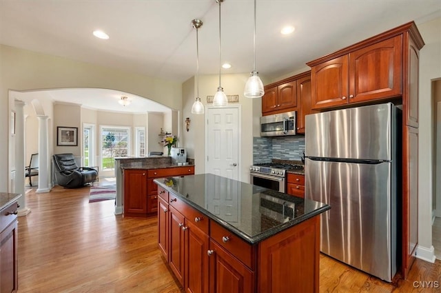 kitchen featuring backsplash, appliances with stainless steel finishes, a center island, arched walkways, and light wood-style floors