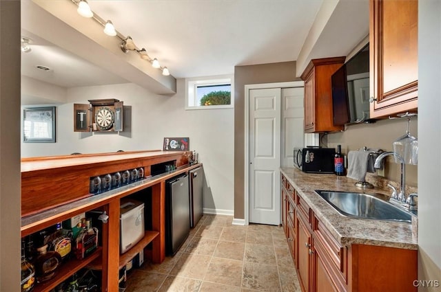 kitchen with black microwave, light stone countertops, brown cabinets, a sink, and baseboards