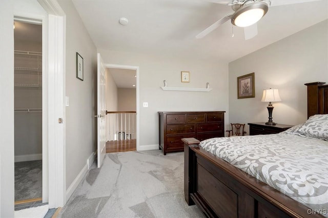 bedroom featuring a closet, baseboards, a walk in closet, light colored carpet, and a ceiling fan