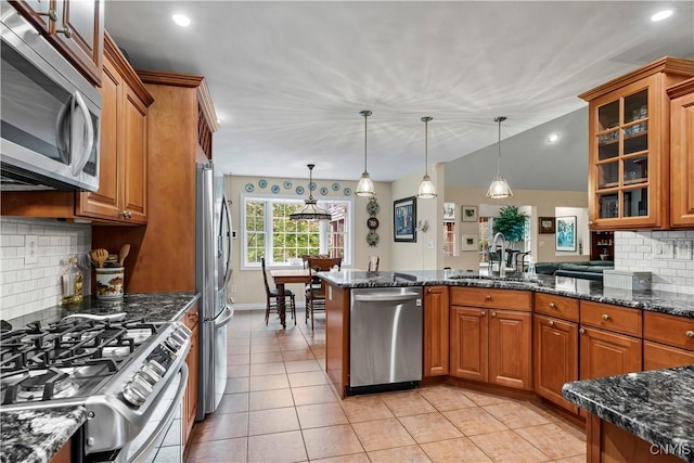 kitchen featuring brown cabinetry, glass insert cabinets, dark stone counters, a sink, and stainless steel appliances