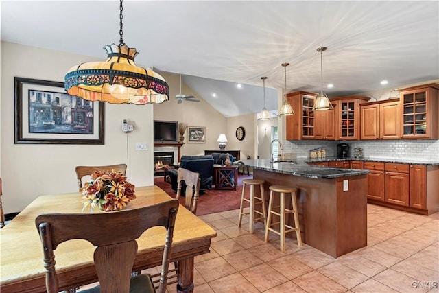 kitchen featuring a sink, a breakfast bar area, brown cabinetry, dark stone countertops, and open floor plan