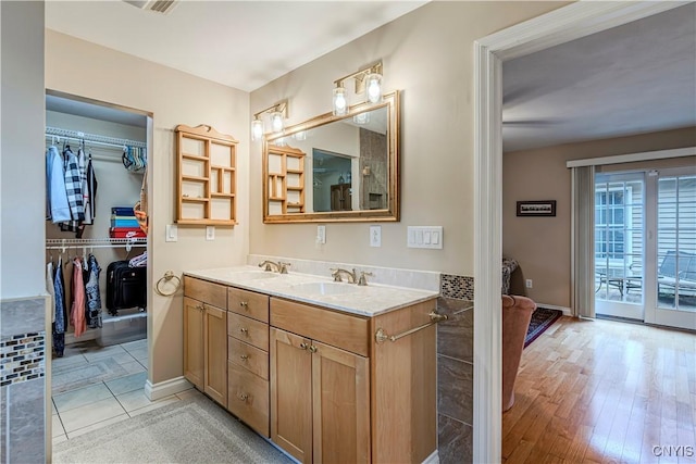 full bathroom featuring double vanity, a walk in closet, a sink, and wood finished floors