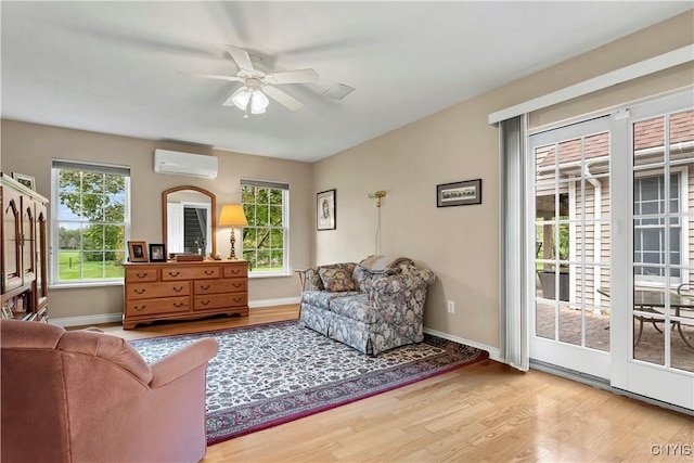 living room featuring a ceiling fan, baseboards, a wall unit AC, and wood finished floors