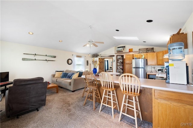 interior space featuring light colored carpet, a breakfast bar, freestanding refrigerator, a ceiling fan, and lofted ceiling with skylight