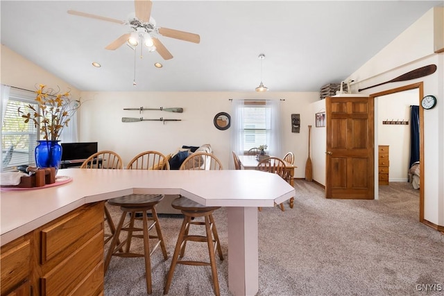 kitchen with a kitchen bar, light colored carpet, light countertops, a ceiling fan, and vaulted ceiling