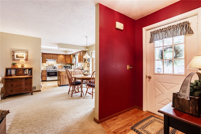 doorway to outside featuring light wood-style floors, baseboards, light carpet, and a textured ceiling
