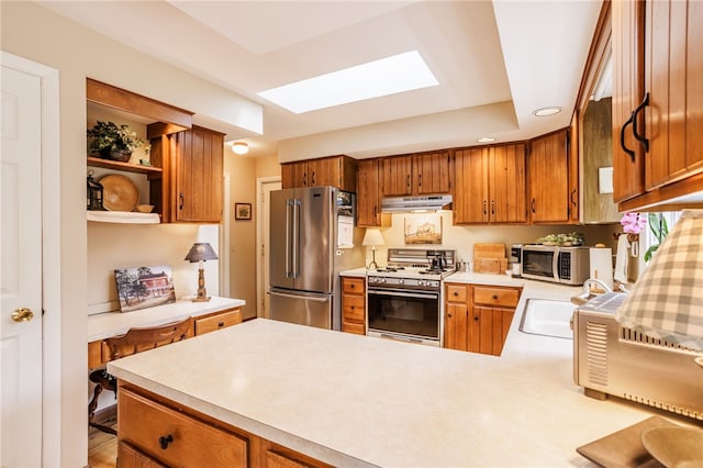 kitchen with a sink, light countertops, freestanding refrigerator, under cabinet range hood, and range with gas cooktop