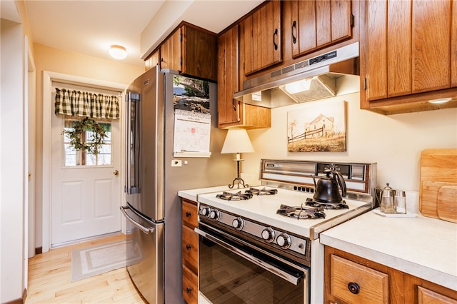 kitchen with under cabinet range hood, brown cabinetry, white range with gas stovetop, and light countertops
