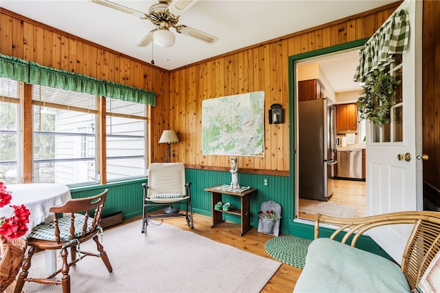 sitting room with light wood finished floors, ceiling fan, and wooden walls