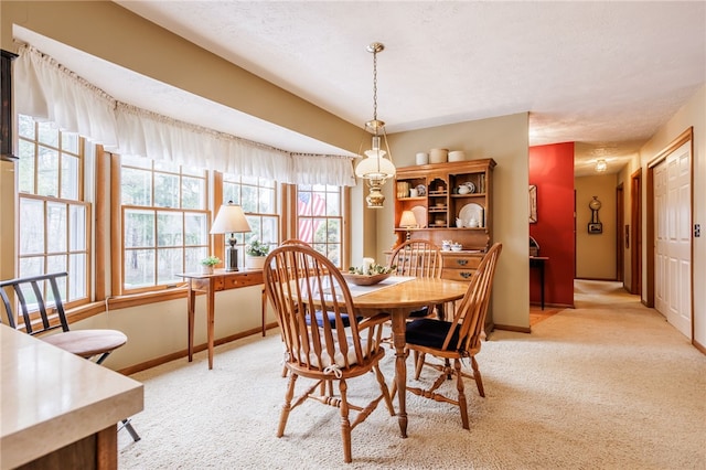 dining space with a textured ceiling, baseboards, and light colored carpet