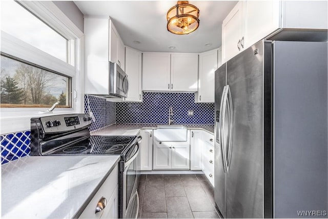 kitchen with a sink, appliances with stainless steel finishes, dark tile patterned floors, and white cabinetry