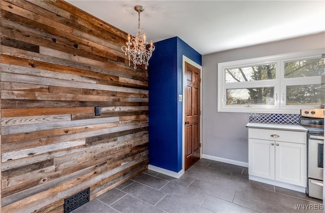unfurnished dining area featuring wooden walls, an inviting chandelier, baseboards, dark tile patterned floors, and visible vents