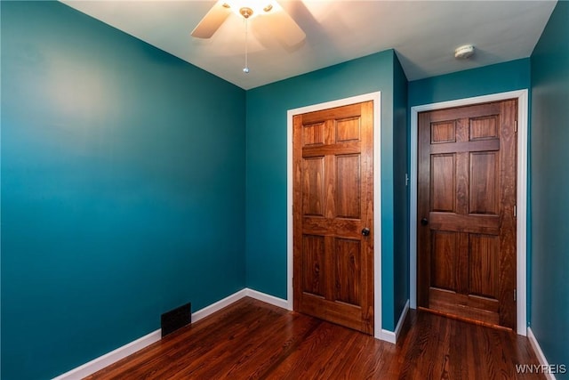 interior space with baseboards, ceiling fan, dark wood-style floors, and visible vents